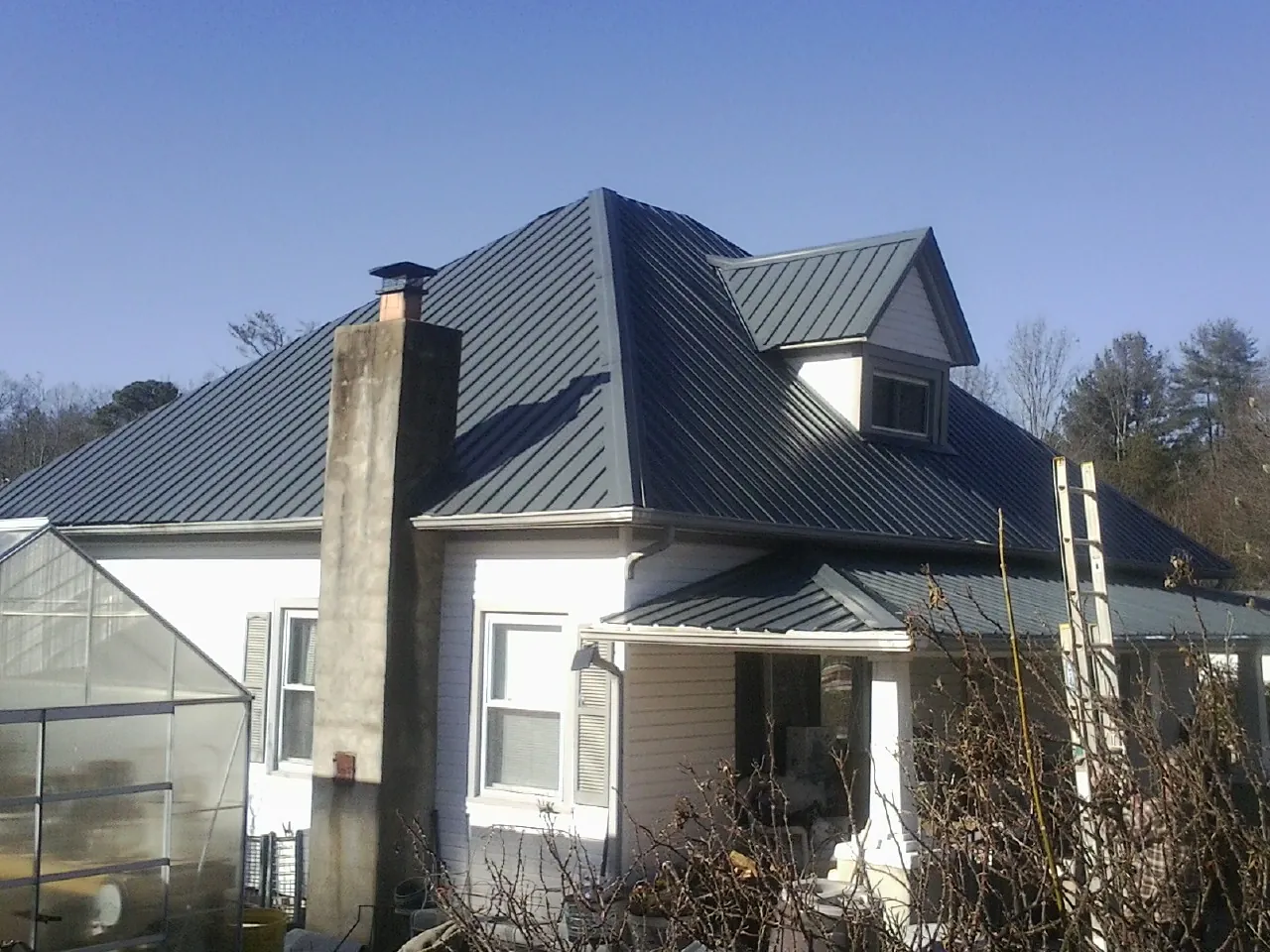 Dark blue standing seam metal roof on a white farmhouse with dormer — Slate & Tile Roof Repair by Roofing Brothers in Catoosa