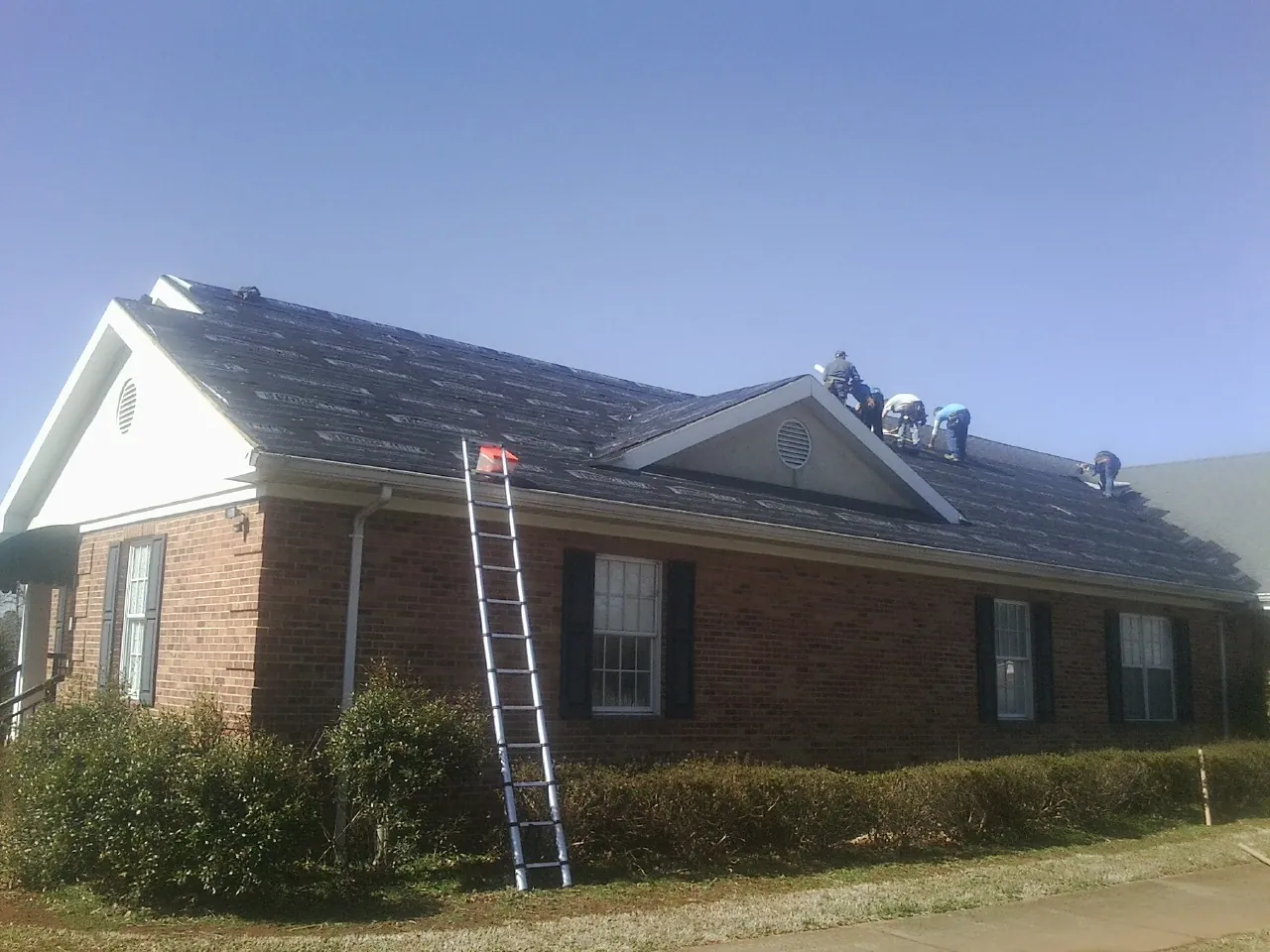 Crew tearing shingles off a brick ranch roof with a ladder set — Emergency Roof Repair work by our crew in Catoosa