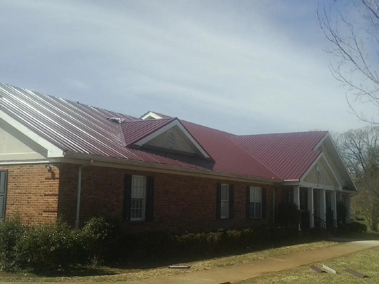 Red metal roof with gabled entries on a long brick building, from a Hail Damage Roof Repair job in Catoosa