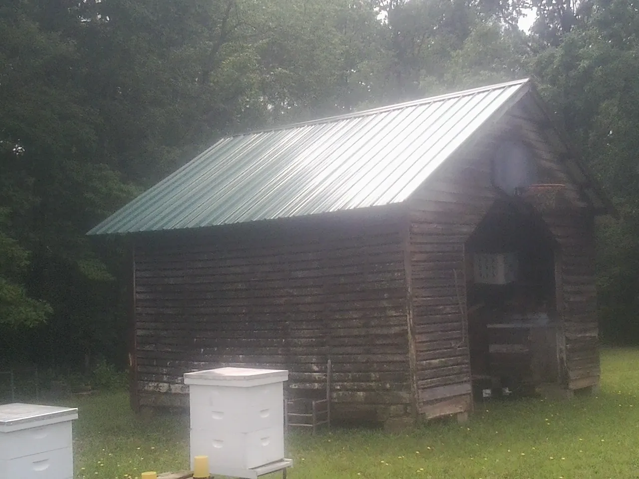 Green metal roof on a weathered barn beside stacked beehives in Catoosa