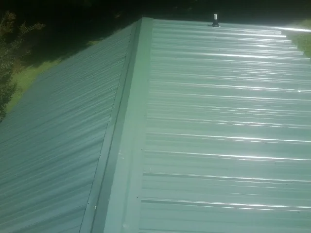 New green metal panels meeting at the ridge of a roof — Flat Roof Repair work by our crew in Catoosa