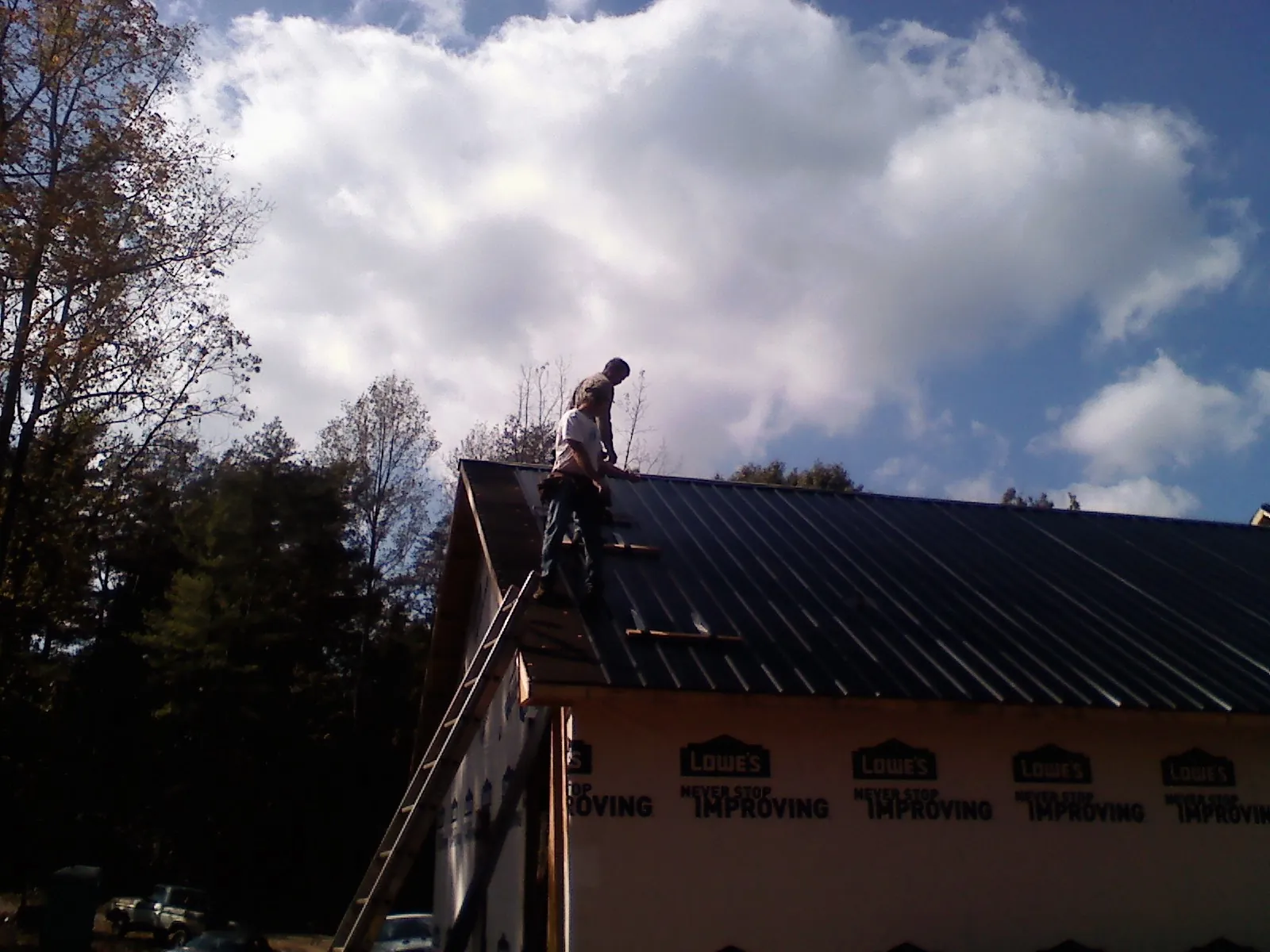Roofer fastening dark metal panels high against a cloudy sky, from a Roof Inspection job in Catoosa