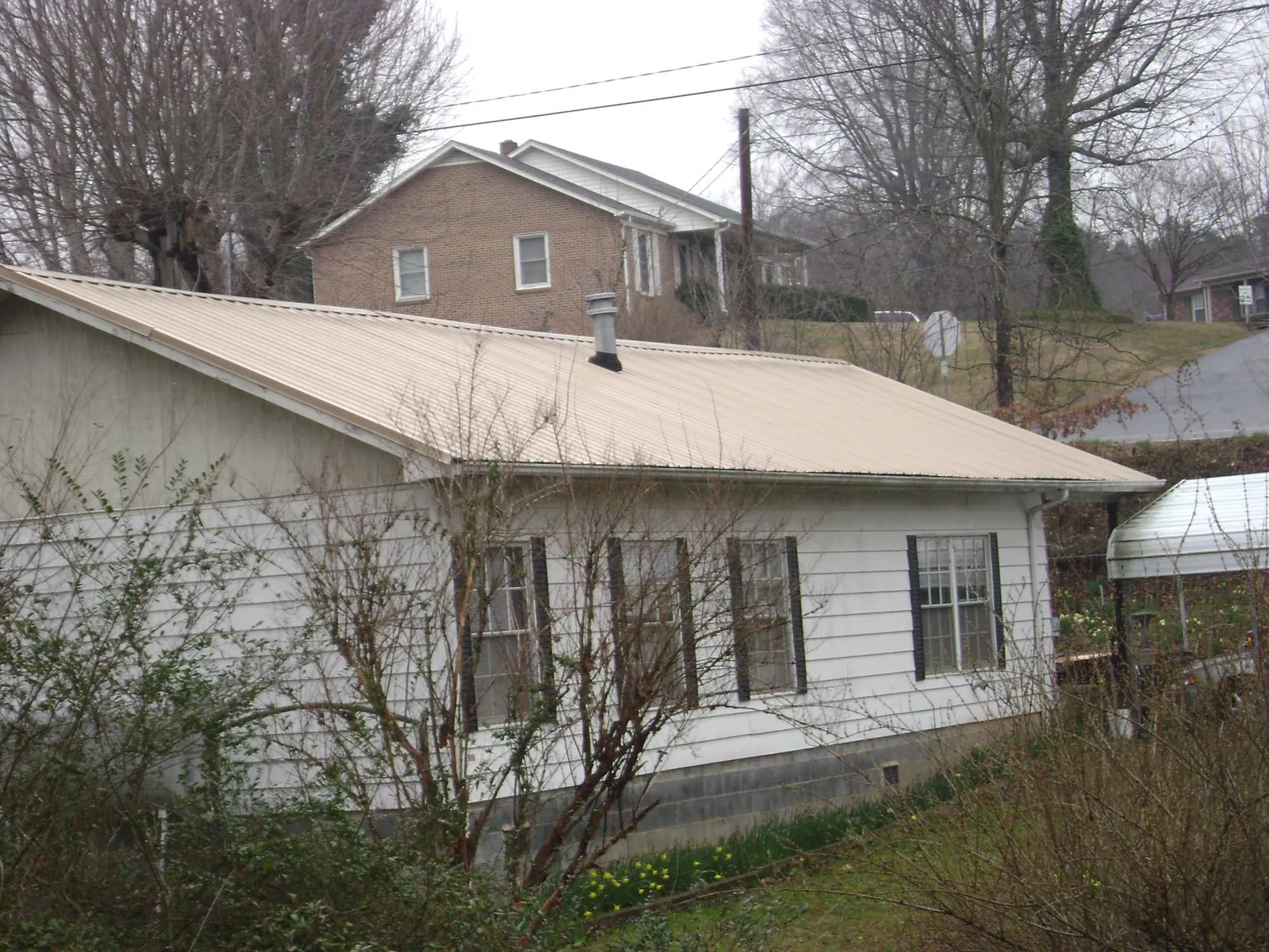 Tan metal roof on a white sided house set into a hillside — Commercial Roofing by Roofing Brothers in Catoosa