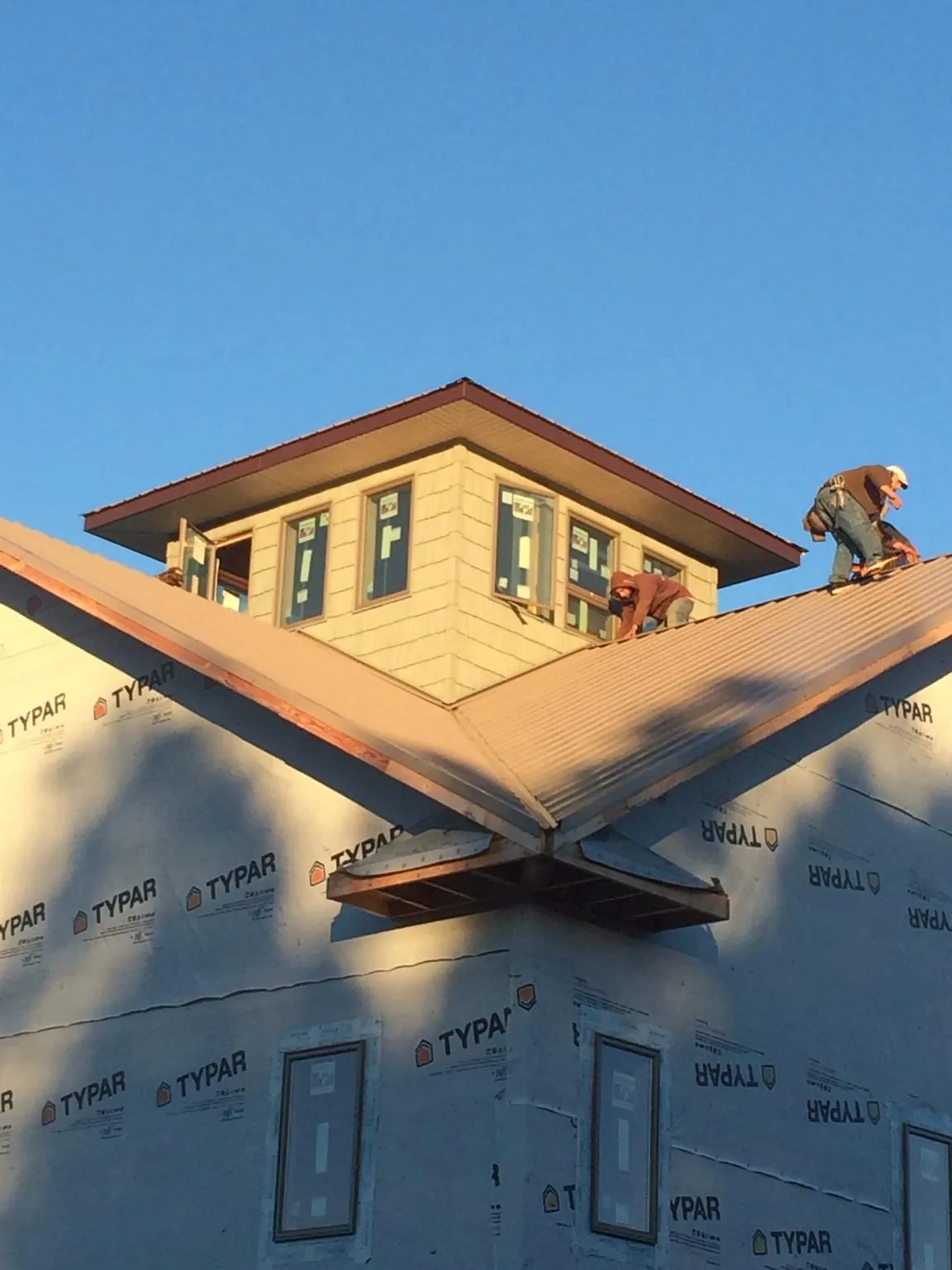 Roofers working around a rooftop cupola on a new metal roof at sunset — Roof Waterproofing in Catoosa by Roofing Brothers